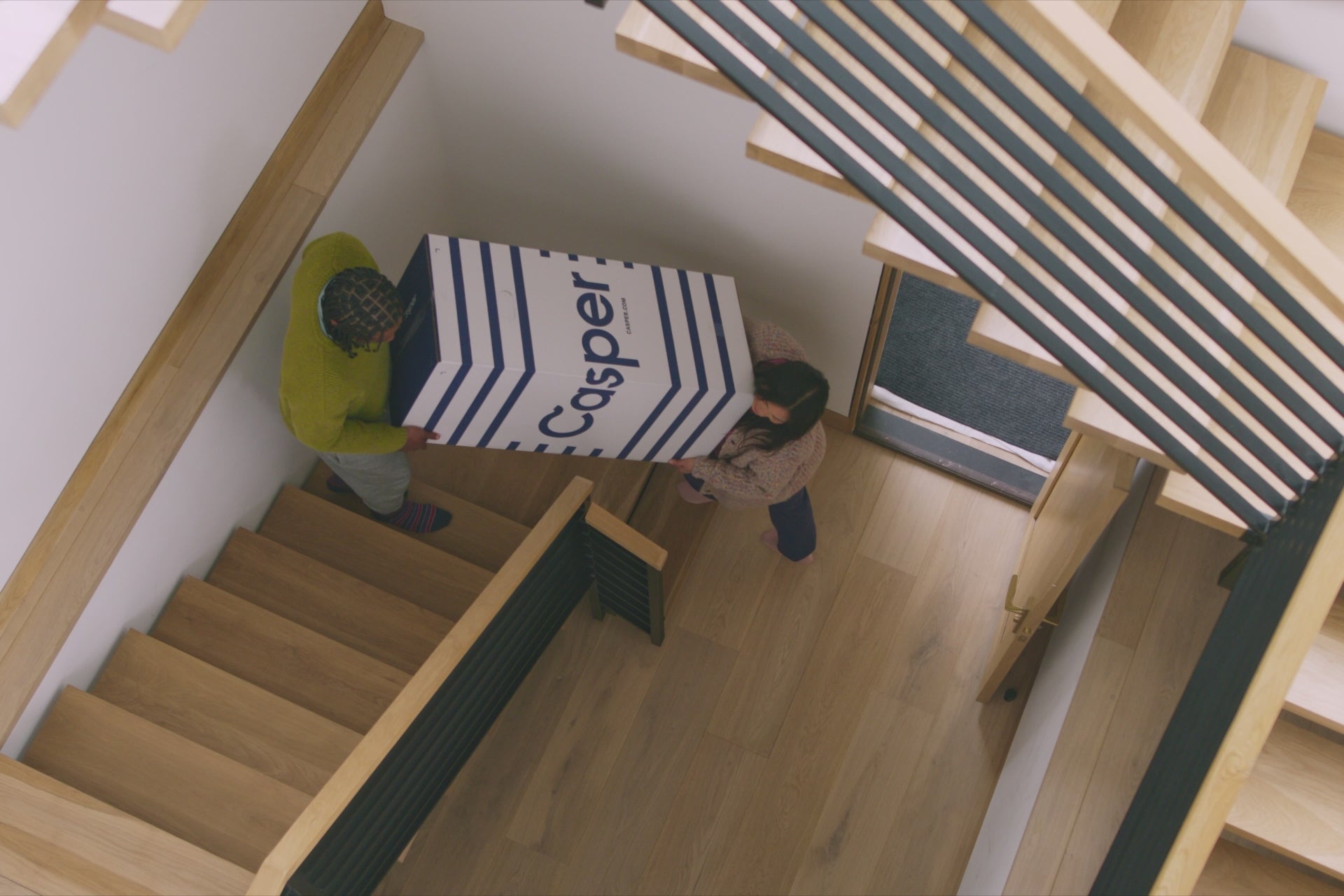 Video of a couple carrying their new Casper mattress in its box up the stairs and setting it up in their bedroom