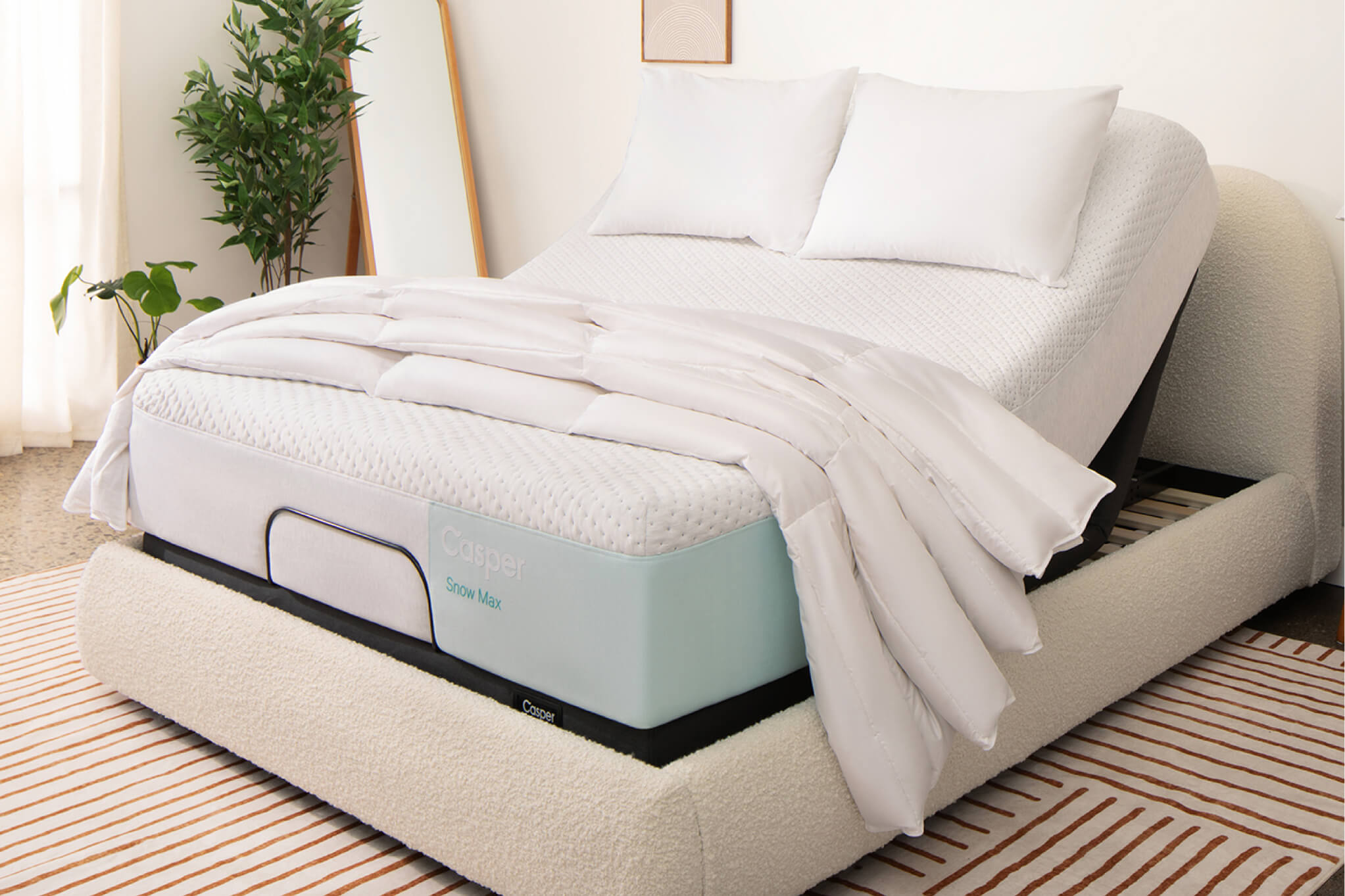 Image of an Adjustable Base Pro with a mattress on top of it. The head of the base is raised, lifting up the head of the mattress for you to be lying upright in your bed. The mattress has two pillows and a folded blanket on top of it.